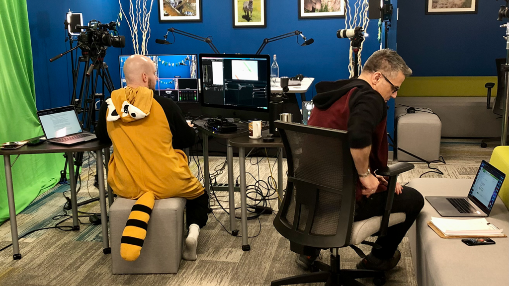 Two Symbiotic Podcast team working on their computers. One is dressed in a Red Panda costume.